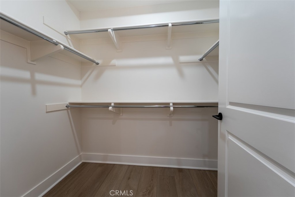 Empty walk-in closet with multiple clothes rods, upper shelves, and wood-look flooring.