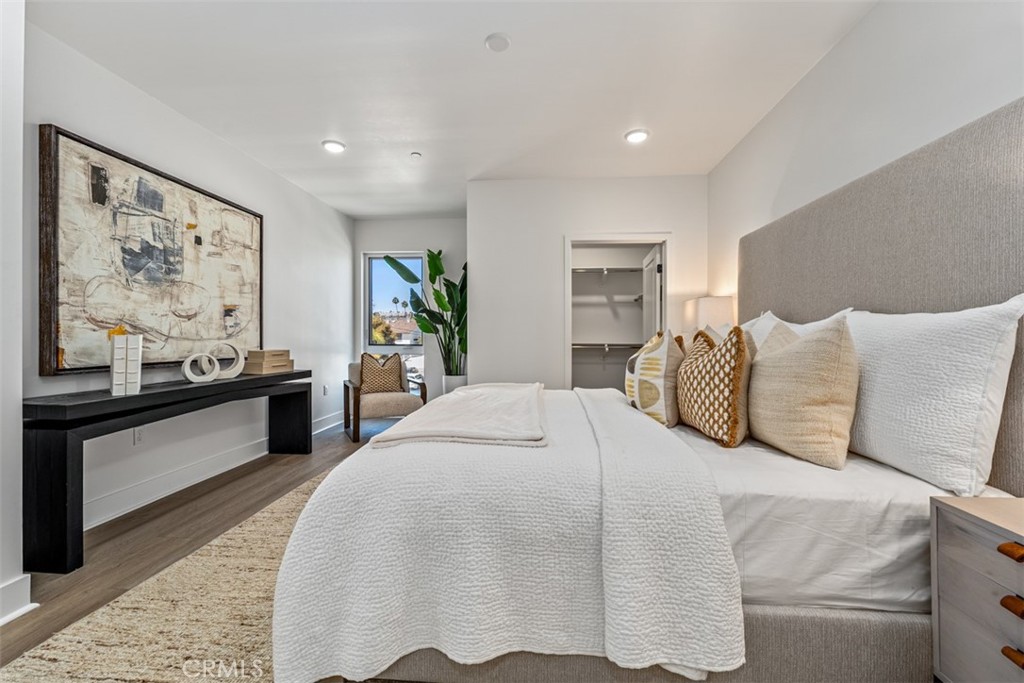 Staged bedroom with white bedding, a gray upholstered headboard, abstract art, and a window.