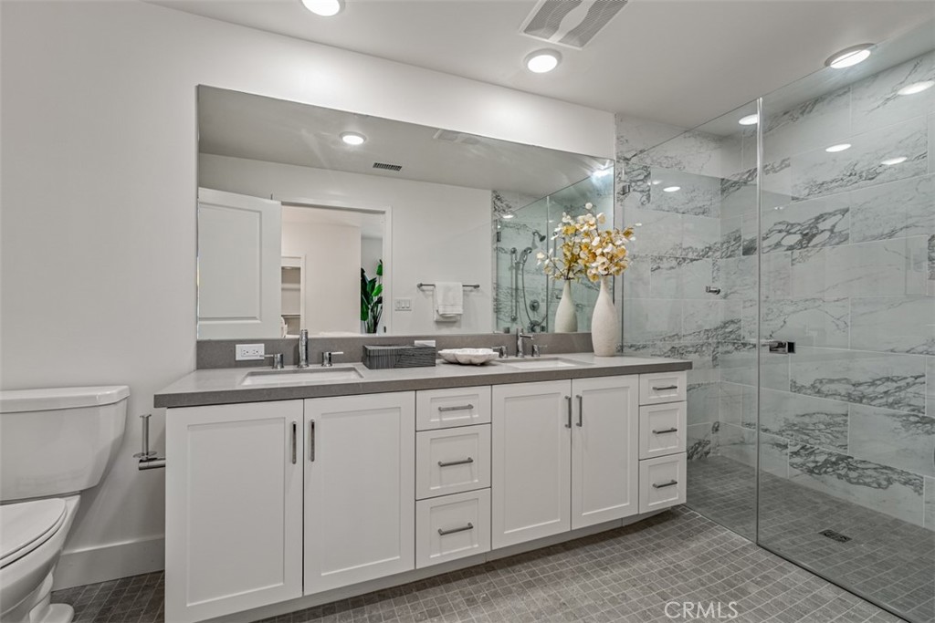 Bathroom with a white double vanity and glass shower lined in gray marble-look tile.