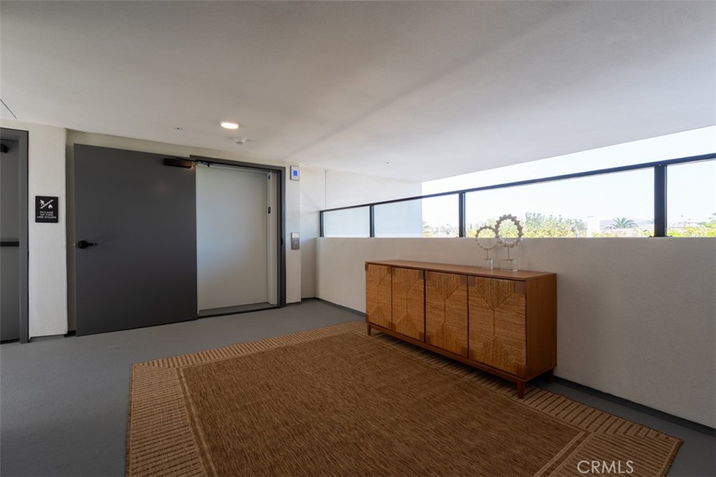 Apartment corridor with a dark entry door, wooden sideboard, woven rug, and long window.