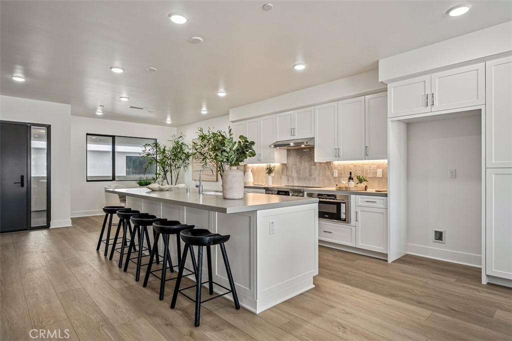 Modern white kitchen with a large island, black bar stools, and wood-look flooring.