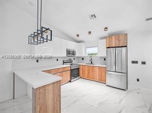 Modern kitchen with wood-front cabinets, stainless steel appliances, and a white peninsula.