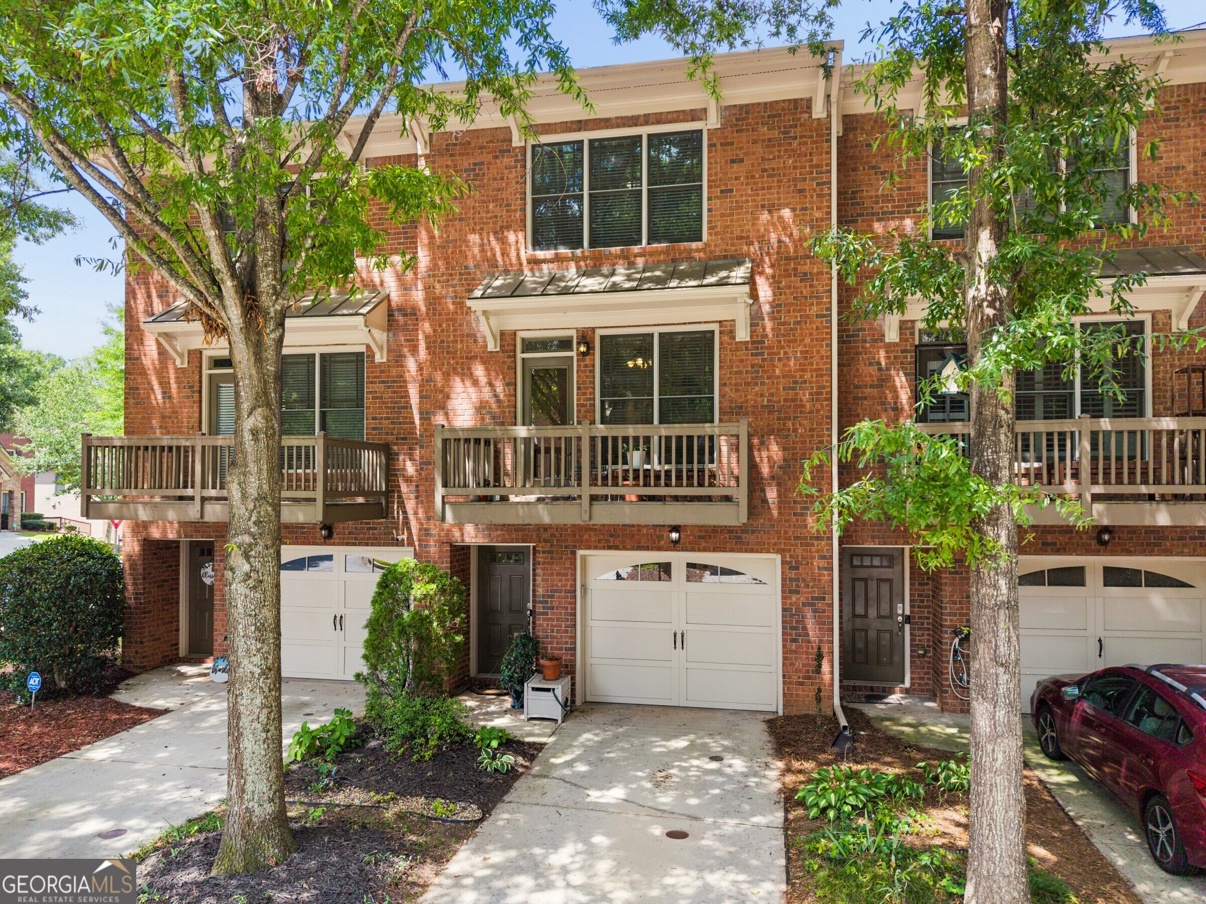Red-brick townhouses with wooden balconies and garages, framed by mature trees.