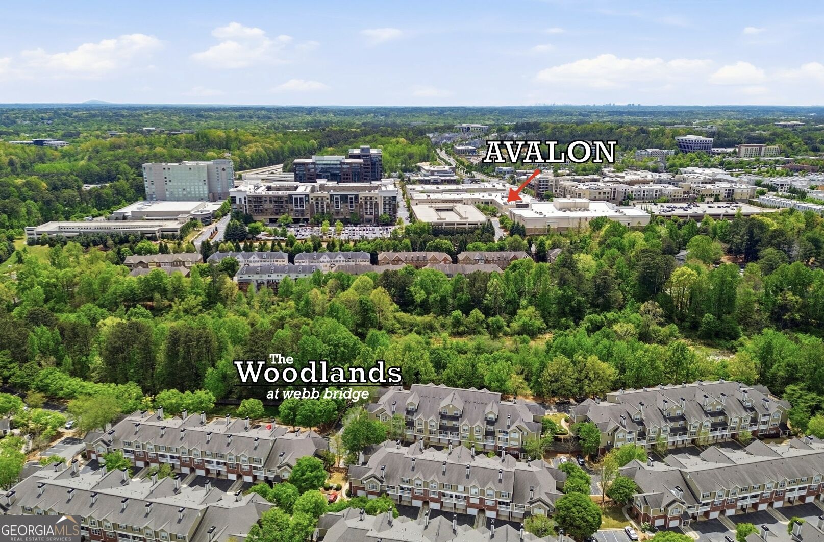 Aerial view of townhomes nestled among trees, with the Avalon district in the distance.