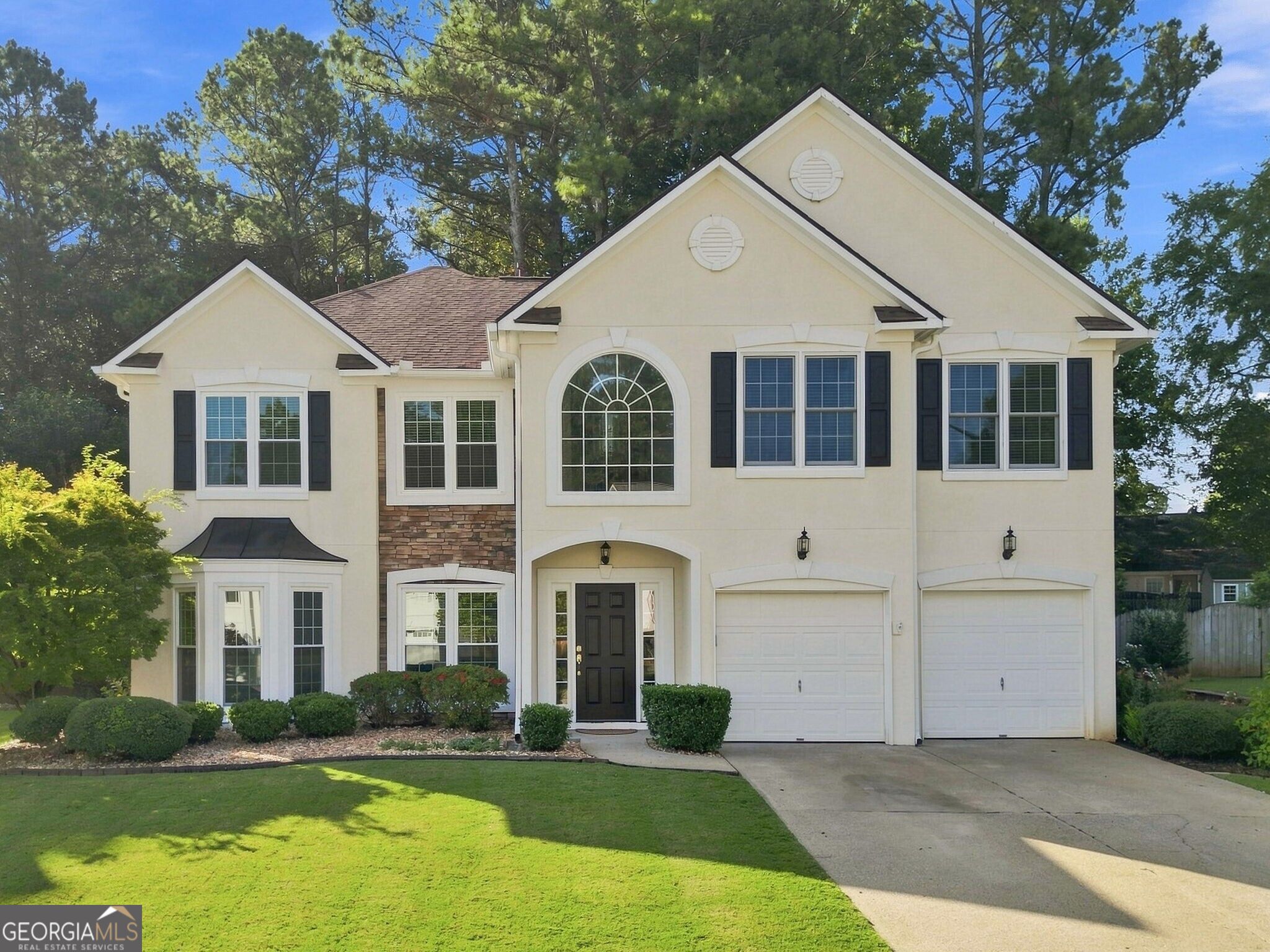Cream two-story house with a prominent arched window, stone accents, and a two-car garage.