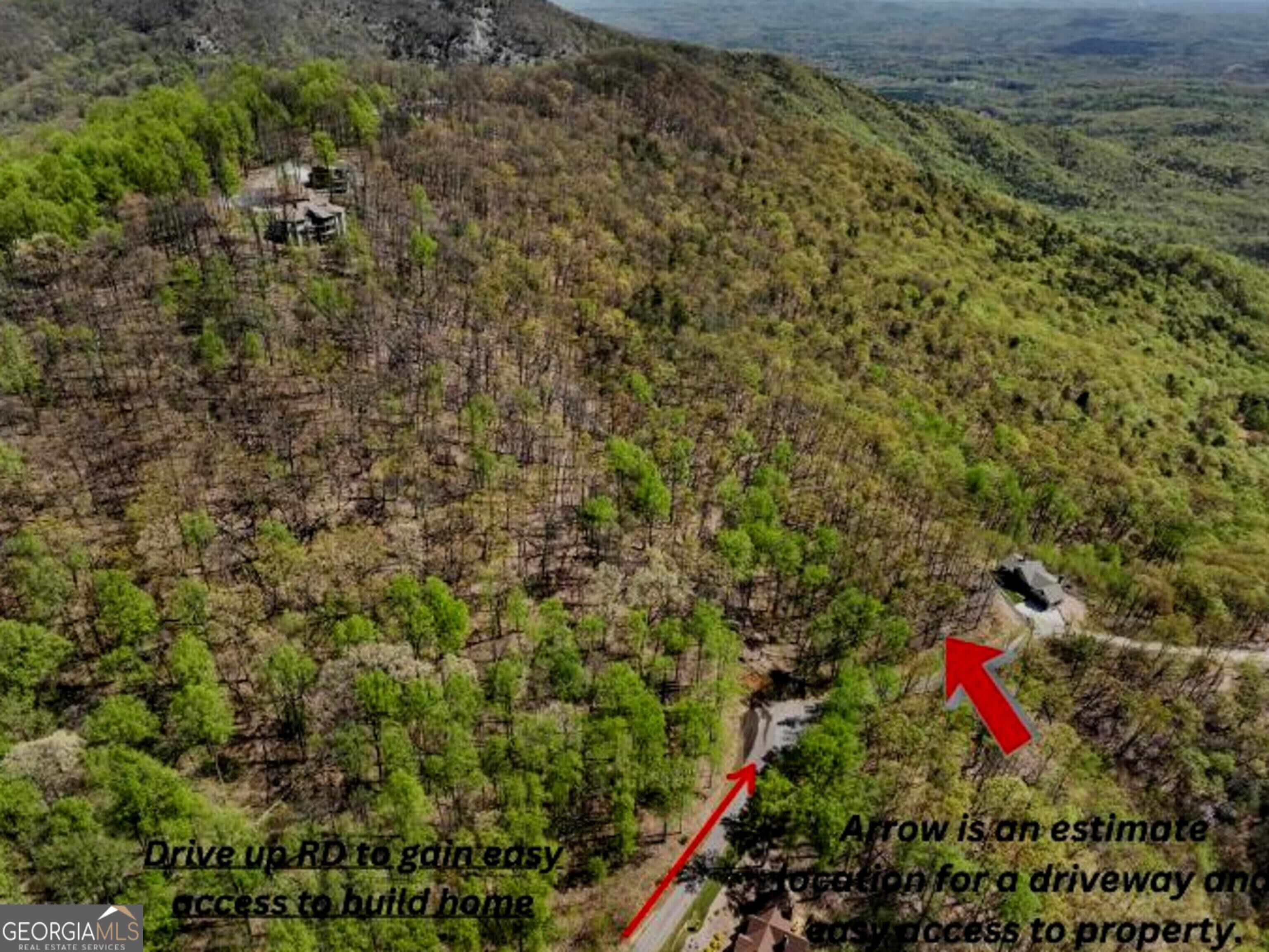 Aerial view of wooded property with road access, buildings, and red arrows marking an estimated driveway.