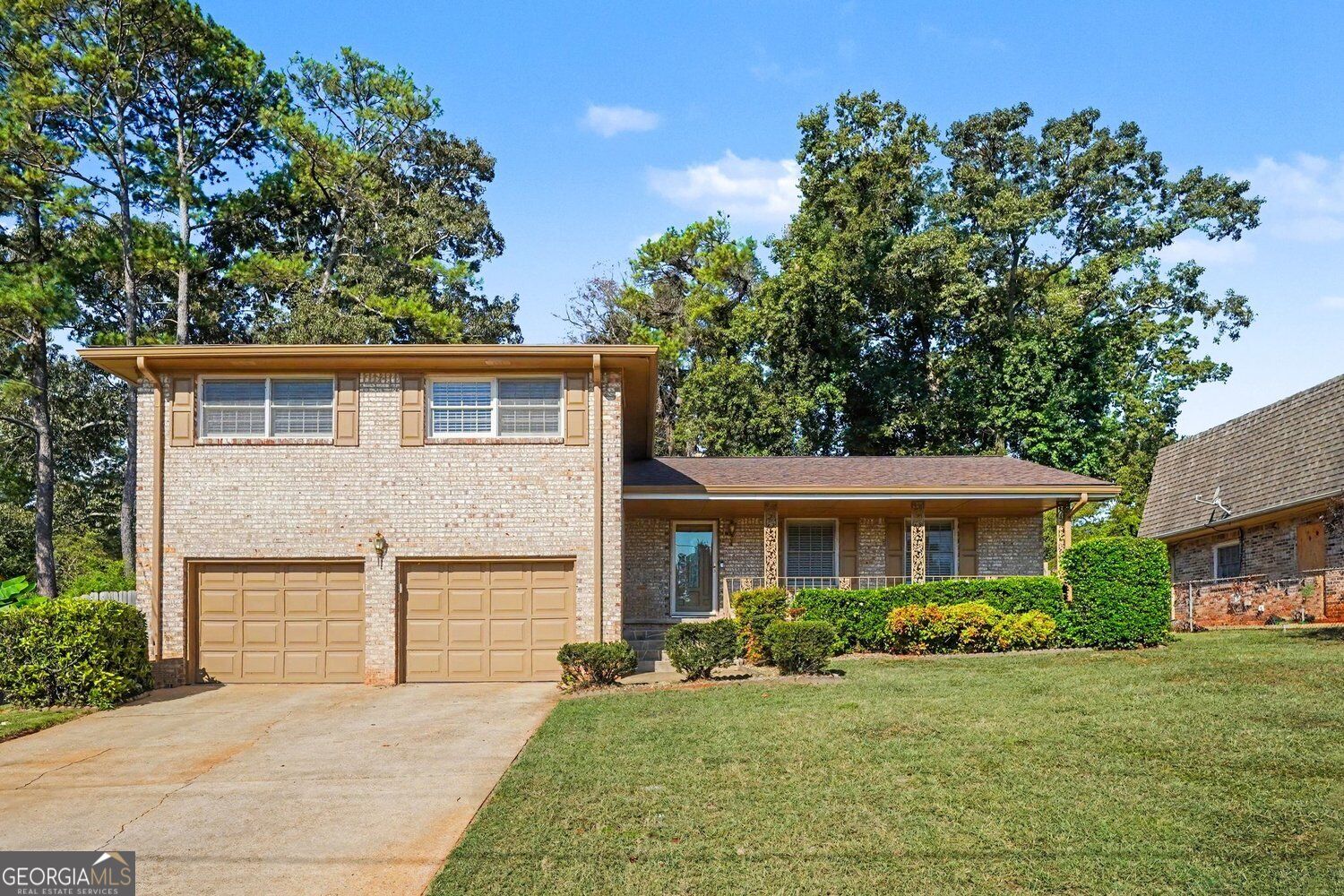 Brick two-story home with twin garage doors, a covered porch, and mature trees.