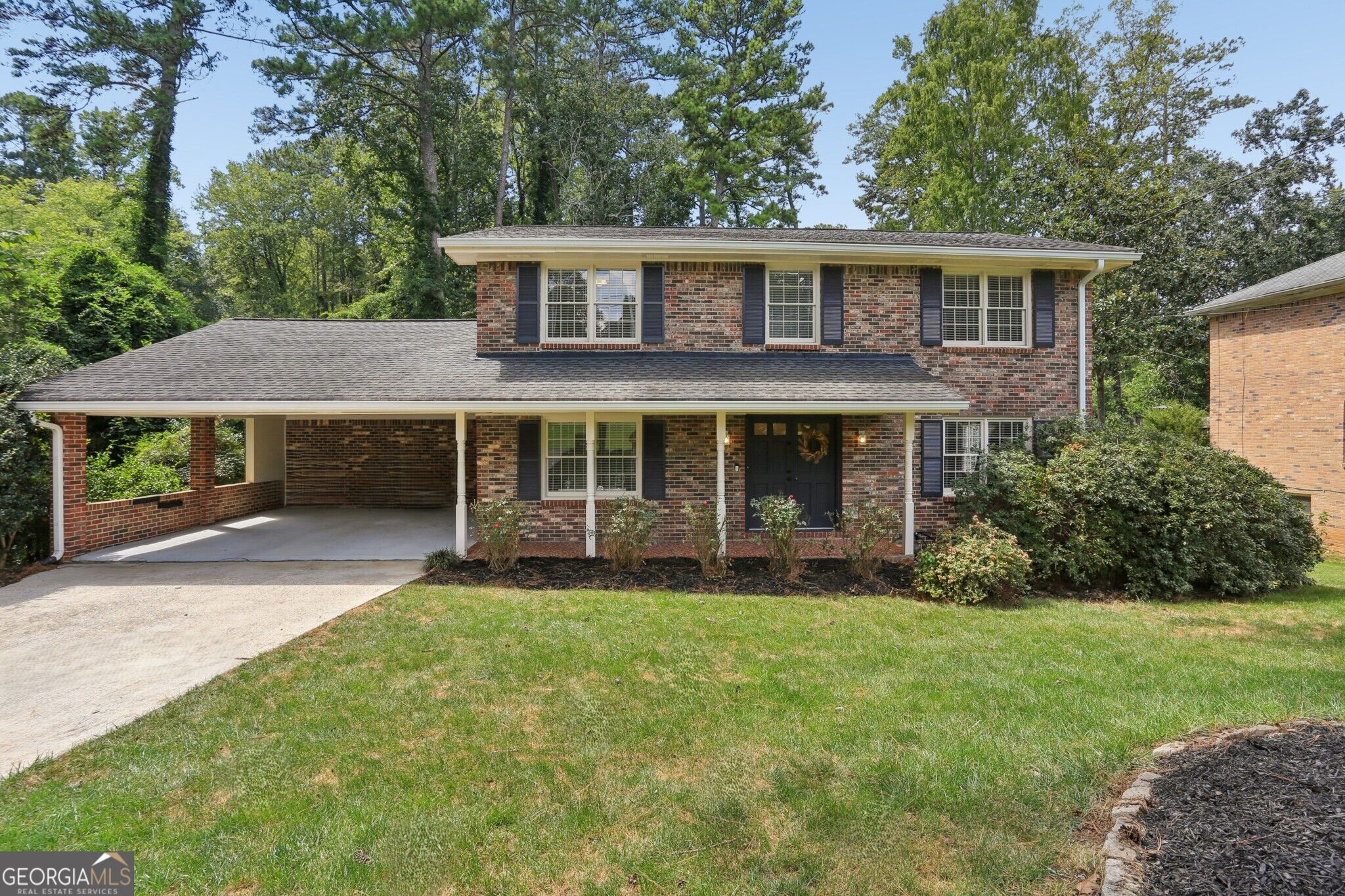 Two-story brick house with a covered carport, front porch, and mature trees.