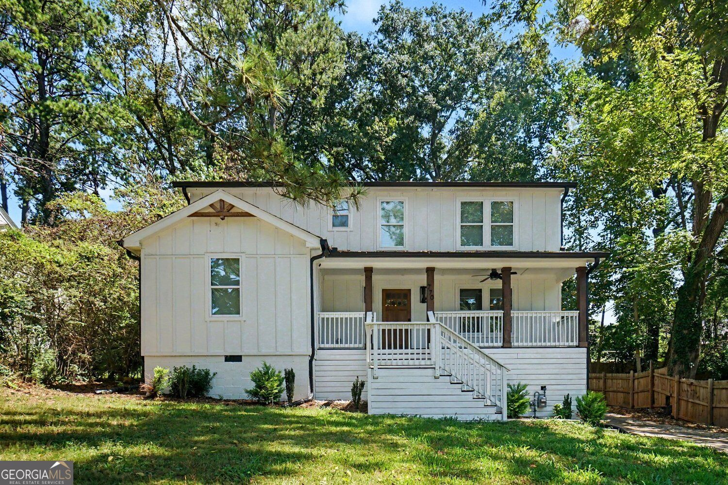 White two-story house with a covered porch and front steps, surrounded by mature trees.