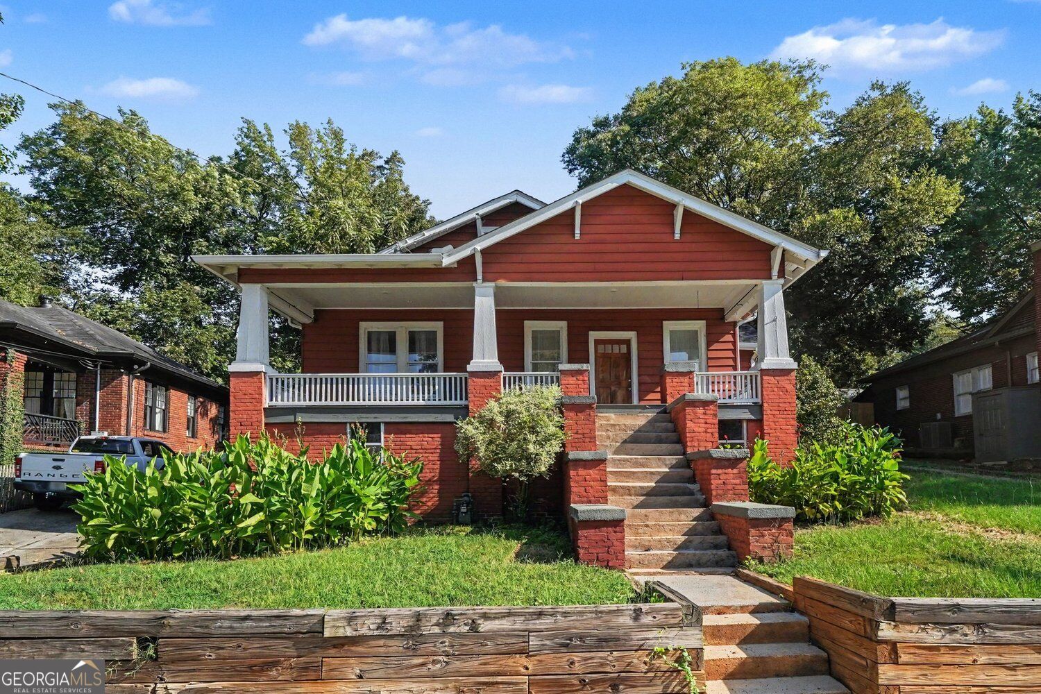 Red-sided, red-brick house with a broad covered porch, white railings, and brick-edged front steps.