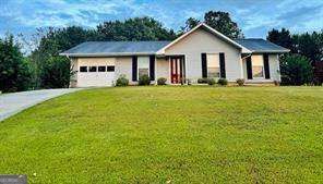 Single-story house with a front porch and attached garage beyond a broad green lawn.