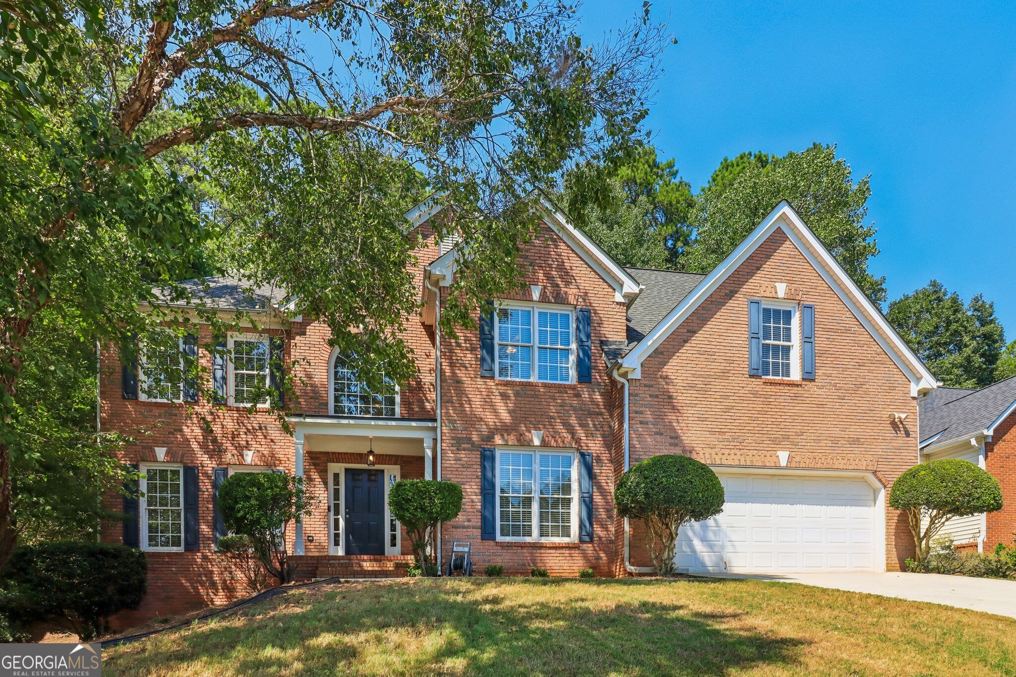 Two-story red-brick house with blue shutters, a covered entry, and an attached double garage.