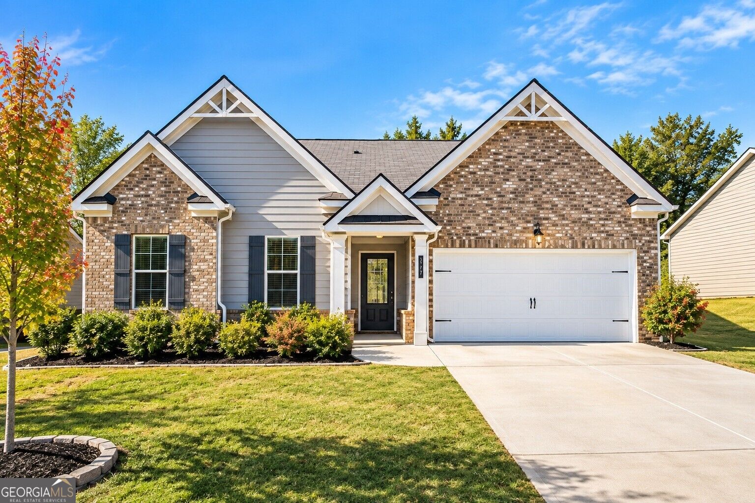 Brick-and-gray-sided home with multiple gables, a wide white garage, and landscaped front lawn.