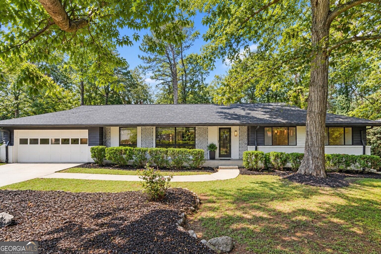 Single-story ranch home with a white garage, dark siding, and mature trees in the front yard.
