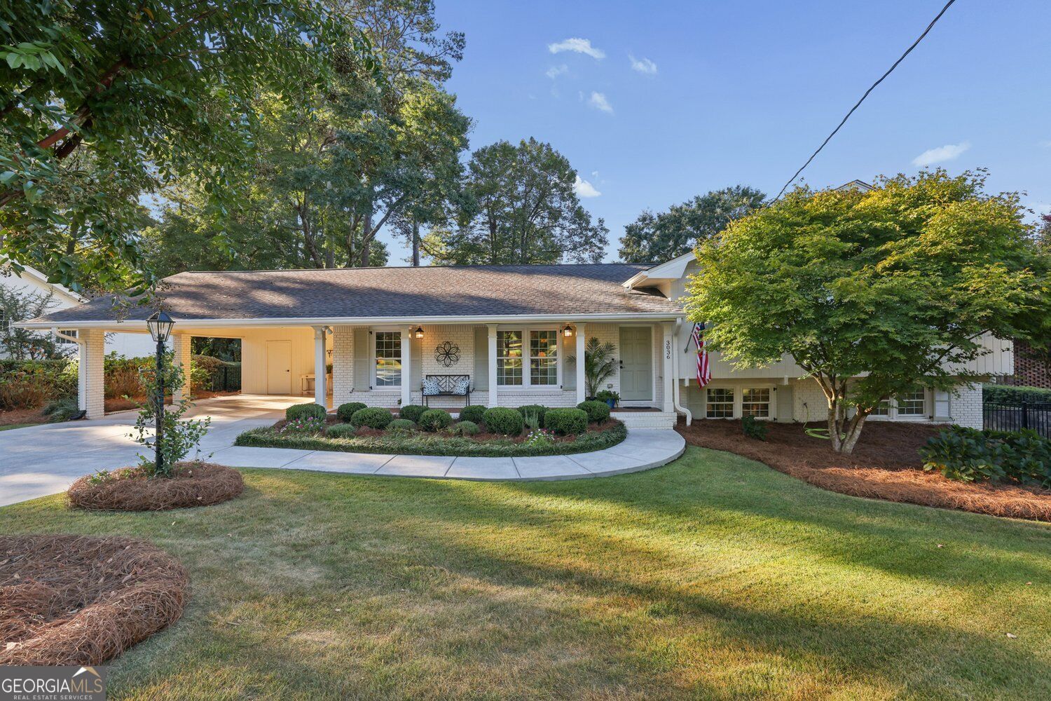 White brick single-story home with a covered porch, curved walkway, and mature trees.