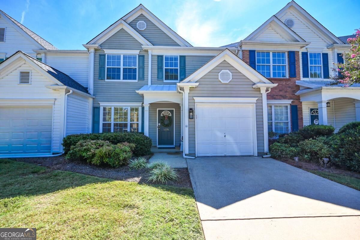 Attached two-story home with gray siding, blue shutters, brick accents, and two garage doors.