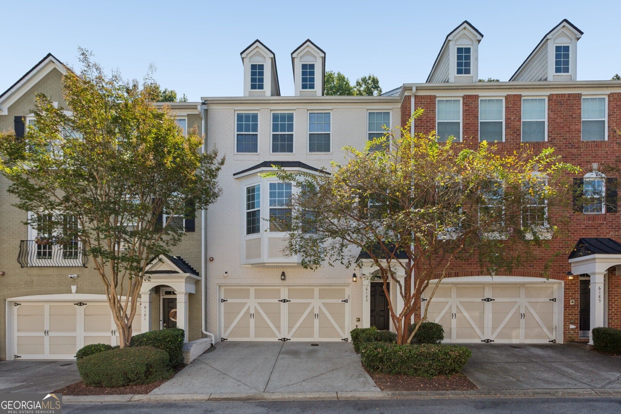 Attached townhouses with white garage doors, varied brick and siding, and tall dormer windows.
