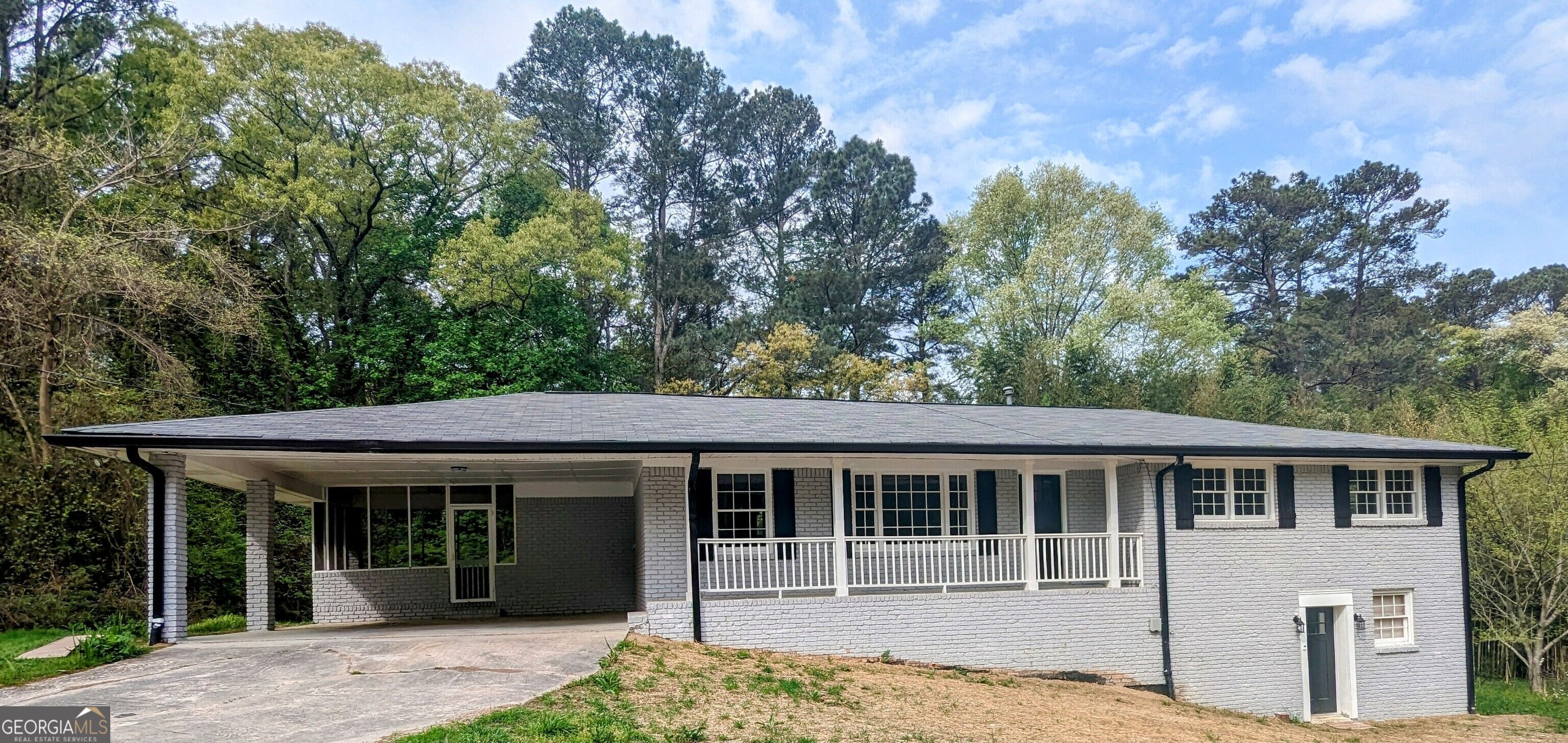 Gray brick home with a covered porch, white railing, and wooded surroundings.
