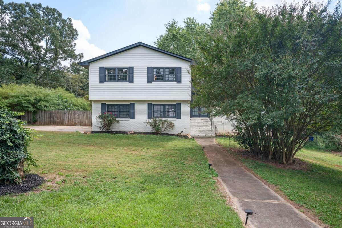 Two-story white house with blue shutters, a front lawn, concrete walkway, and mature trees.