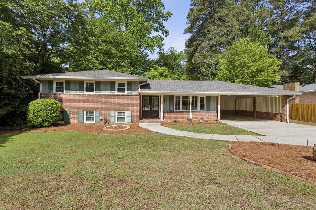 Split-level brick home with an attached carport, broad lawn, and mature trees.