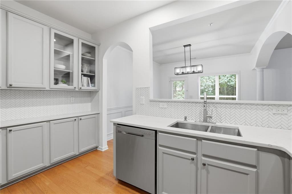 Bright white kitchen with herringbone tile backsplash, glass-front cabinets, and a large island sink.