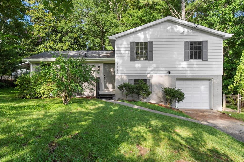 White split-level house with gray shutters, brick lower facade, and a one-car garage amid mature trees.