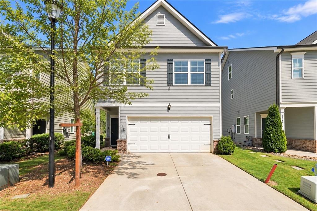 Gray two-story house with an attached double garage, broad driveway, and leafy tree in front.