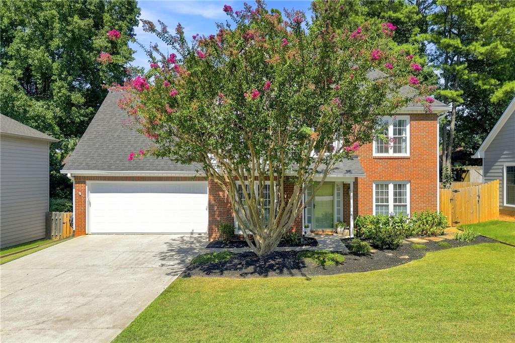 Two-story brick house with a double garage, partly screened by a flowering crepe myrtle.