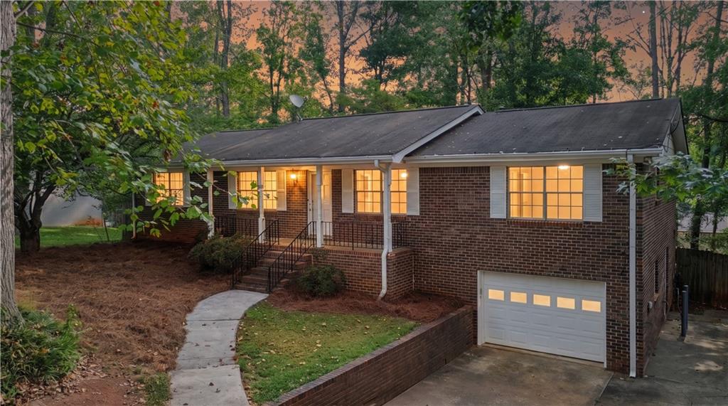Brick home at dusk with warmly lit windows, front steps, and an attached garage.