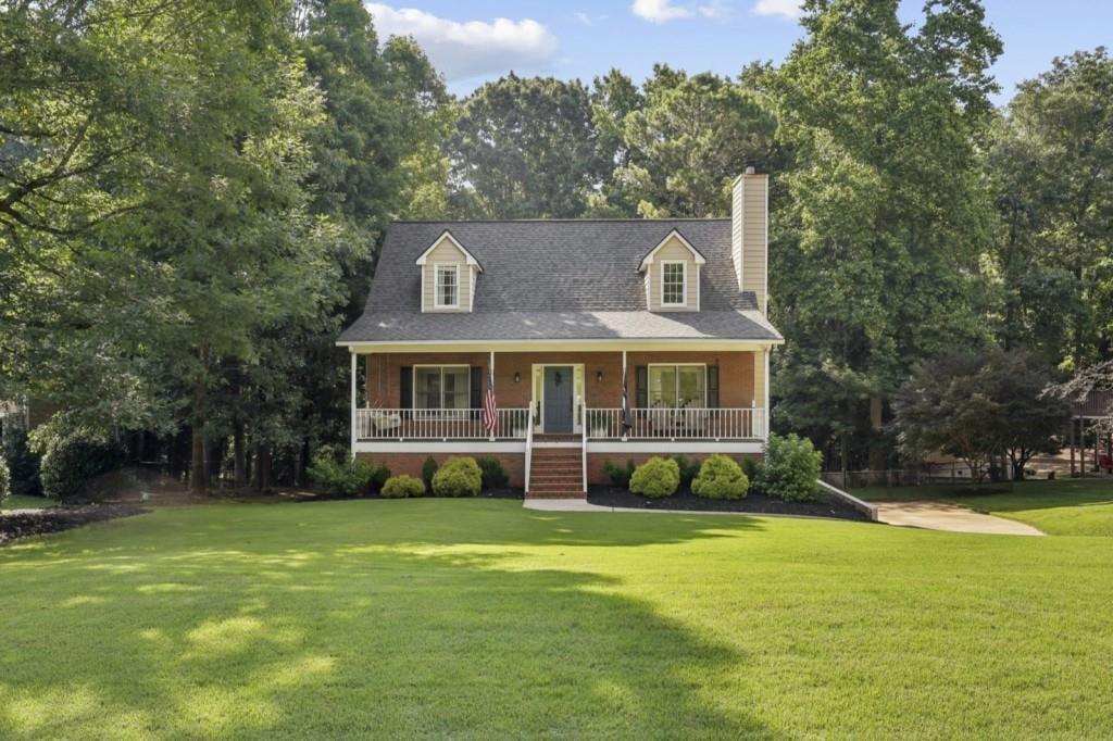 Red-brick house with a broad covered porch and dormer windows, surrounded by trees.