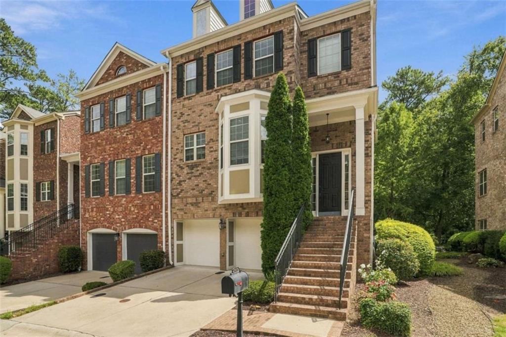Brick townhouse with an attached garage, raised entrance, and landscaped front yard.