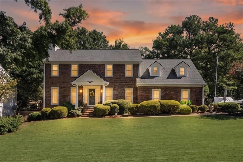 Two-story brick house with dormer windows and a broad manicured lawn at sunset.