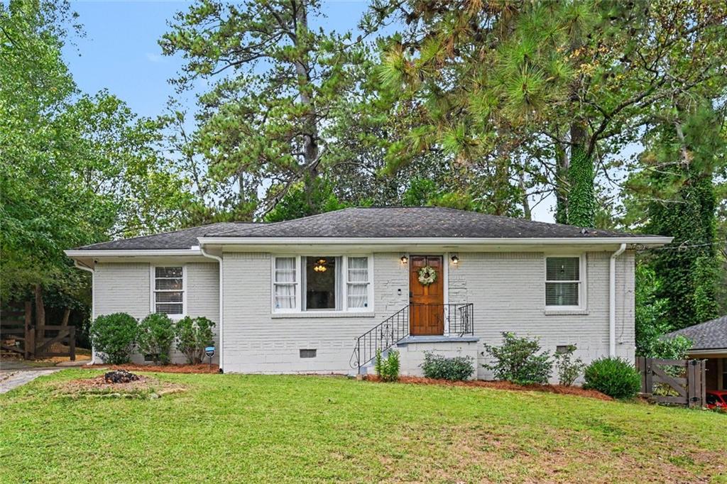 Single-story white brick house with a wooden front door, broad lawn, and mature trees.