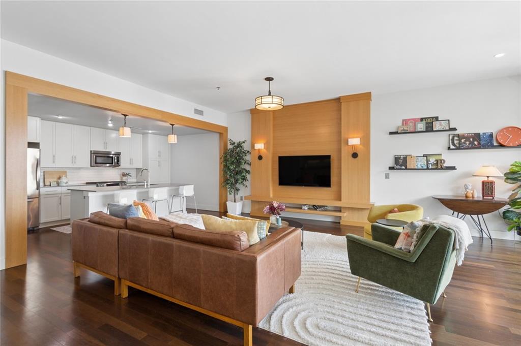 Open-plan living room with a wood-paneled TV wall, leather sofa, and adjoining white kitchen.