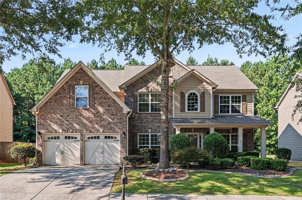 Two-story brick-and-siding home with a two-car garage, covered porch, and large front-yard tree.