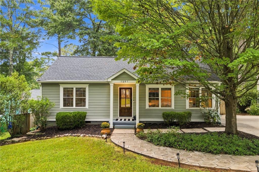 Single-story gray-green home with a covered entry and curved stone walkway beneath leafy trees.