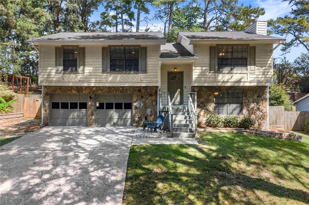 Split-level house with a stone facade, two-car garage, and tree-shaded driveway.
