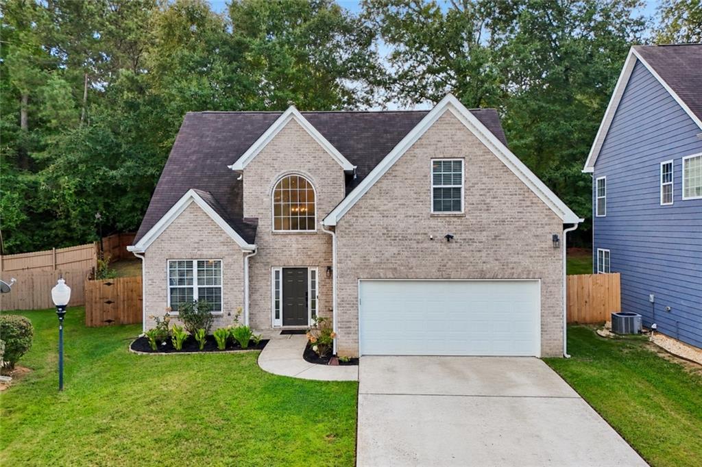Two-story brick house with gabled roof, double garage, landscaped lawn, and concrete driveway.