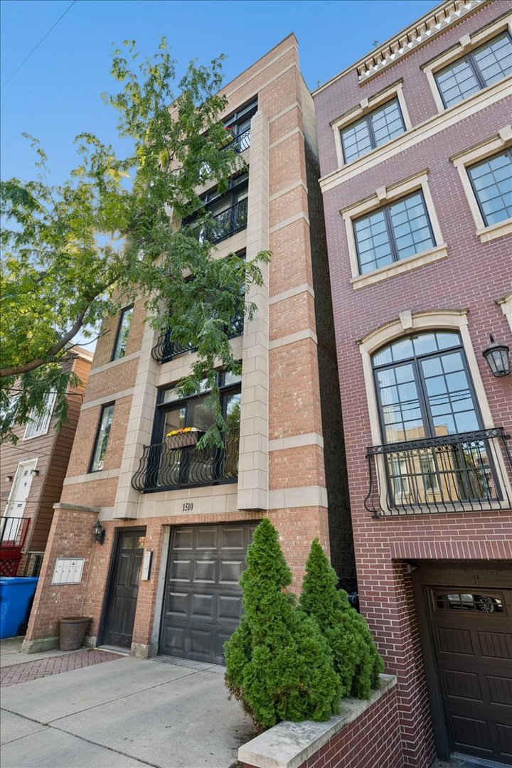 Brick residential building with stone trim, metal balconies, and a street-level garage.