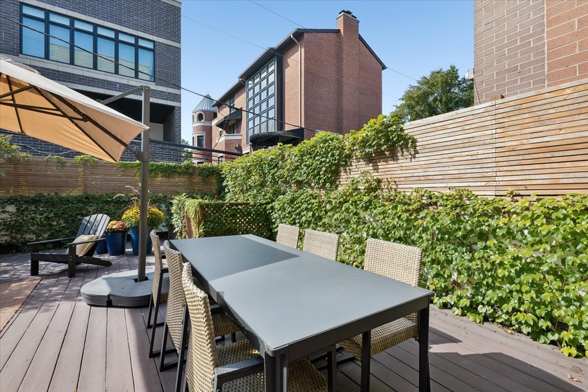 Private patio with a dining table and chairs, tan umbrella, and ivy-covered fencing.