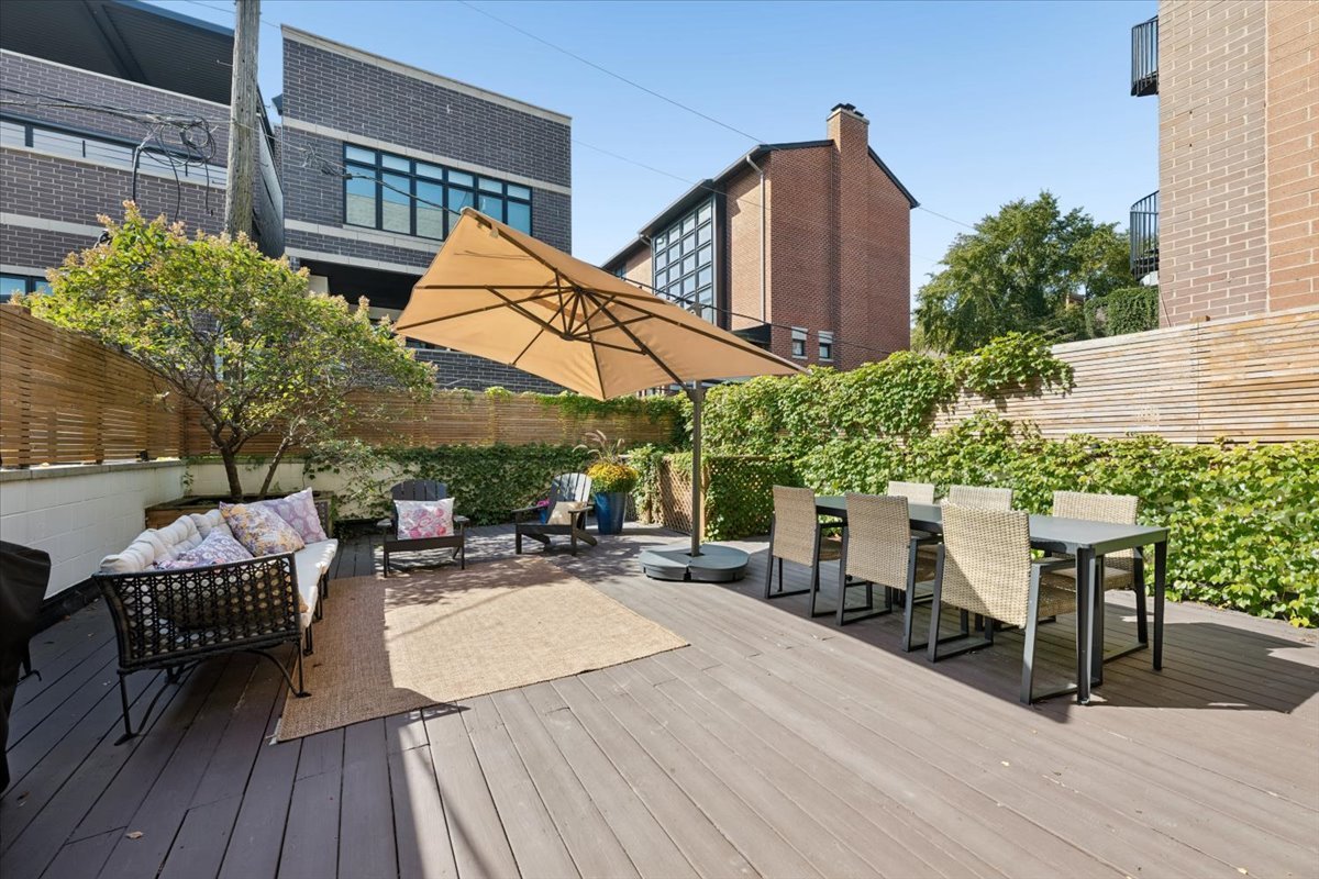 Furnished wooden patio with dining set, cushioned lounge seating, and a large tan umbrella.