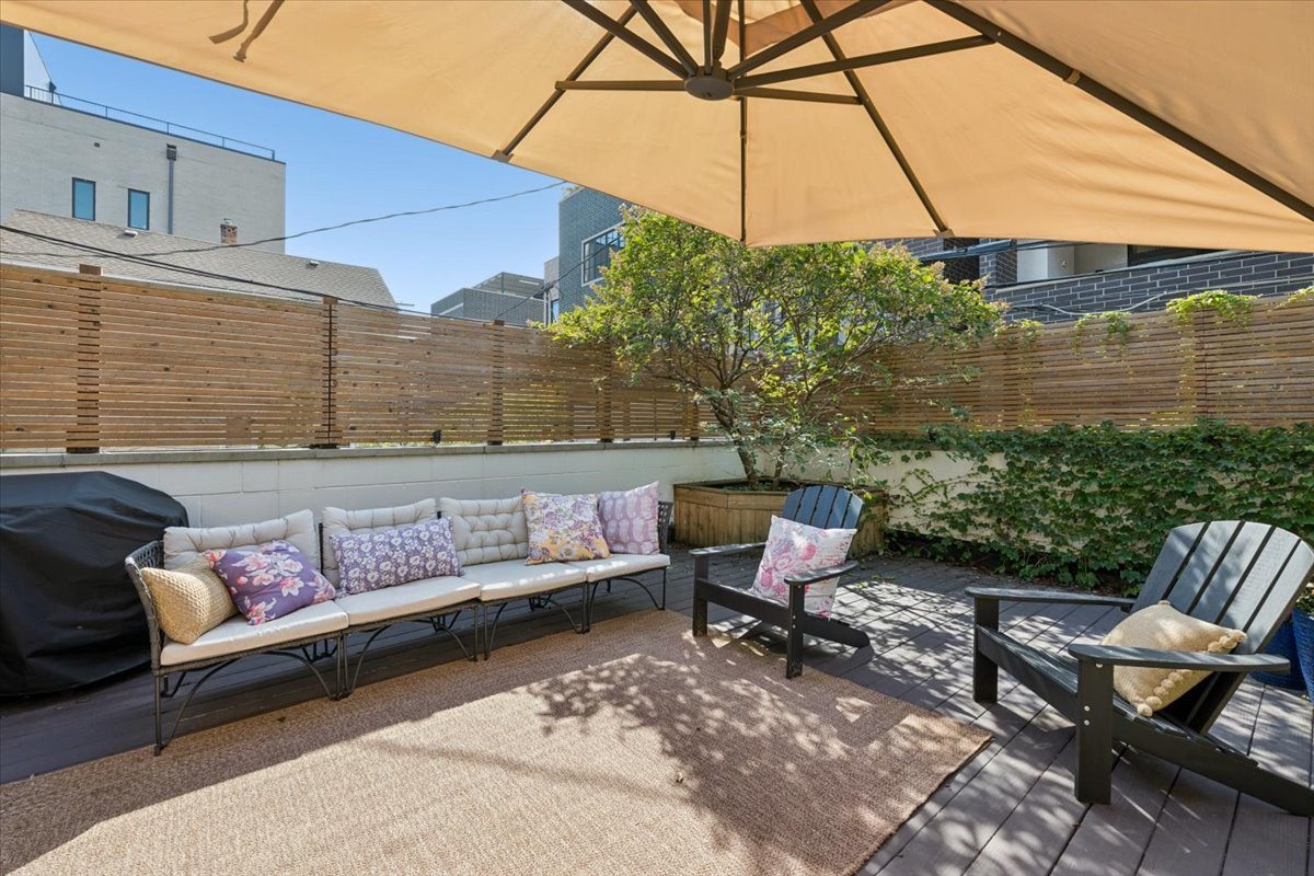 Private patio with umbrella-shaded lounge seating, a potted tree, and wooden privacy fence.
