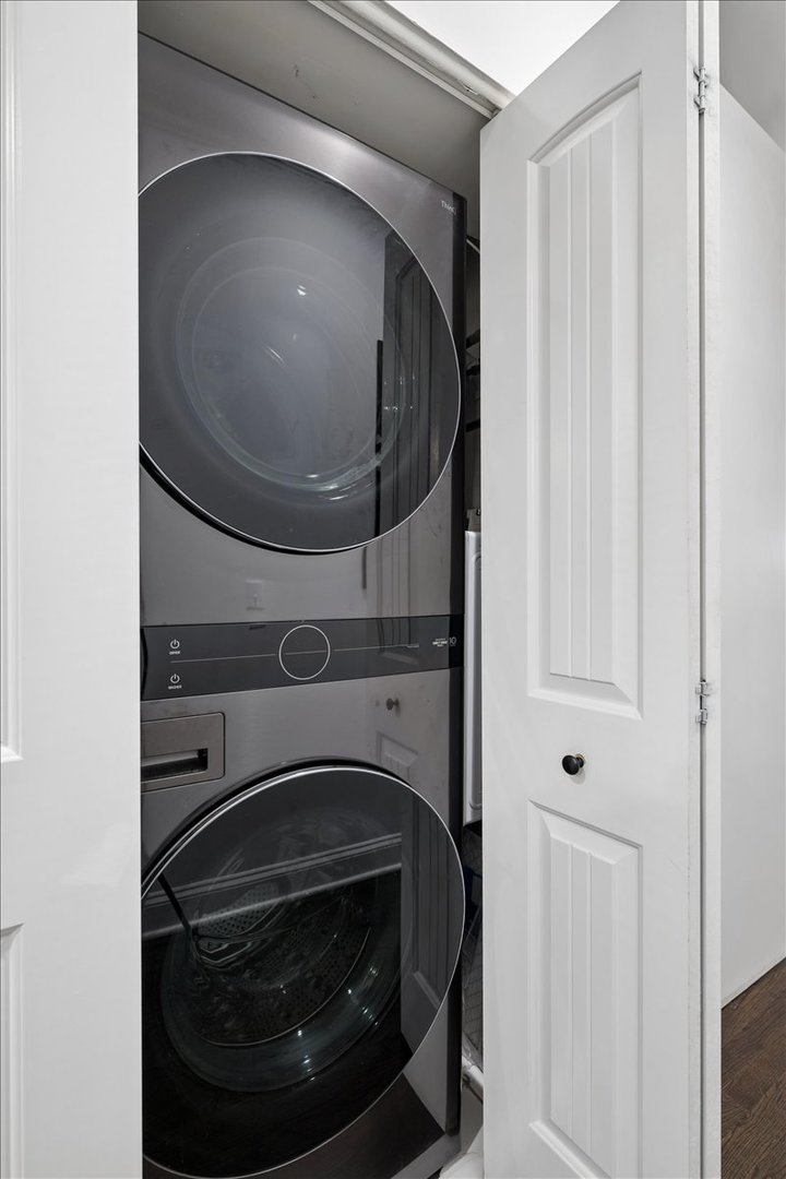 Stacked front-loading washer and dryer inside a closet behind an open white door.