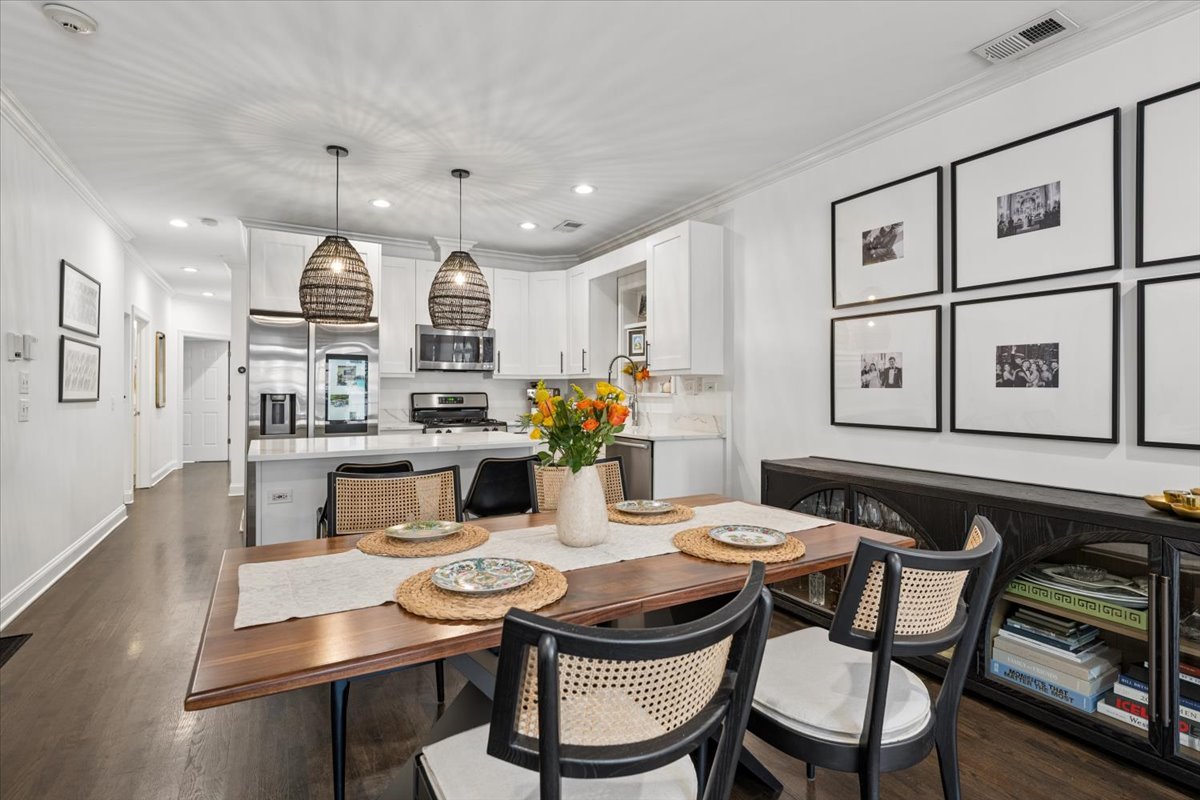 Open-plan kitchen and dining area with white cabinets, stainless appliances, and a large wood table.