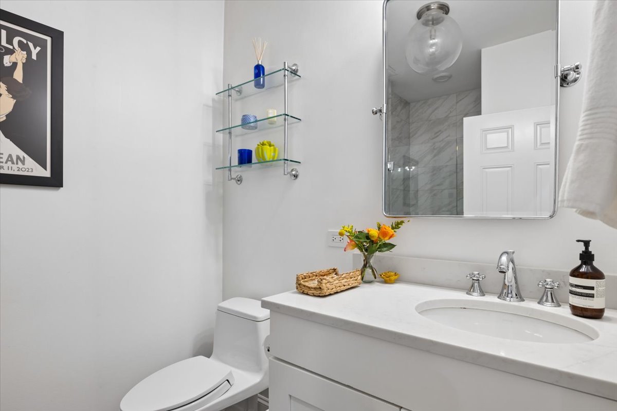 Bathroom with a white vanity, large mirror, toilet, and marble-tiled shower reflected in the mirror.