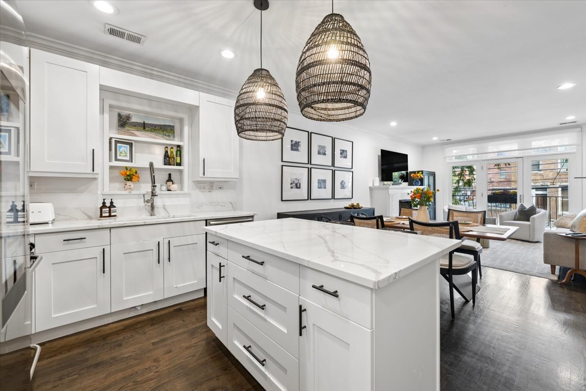 Open-plan kitchen with a large white island, woven pendant lights, and living area opening to a balcony.