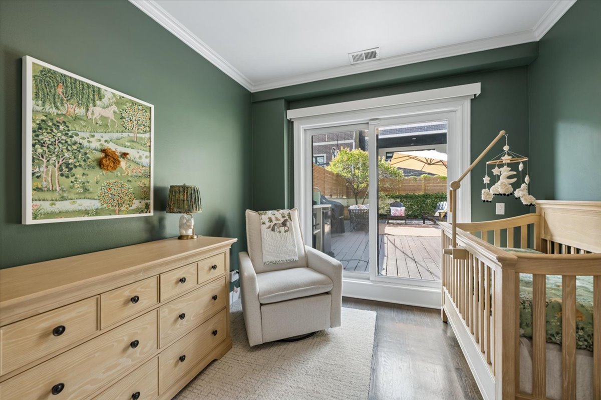 Nursery with a wooden crib, cream glider, and sliding glass doors opening to a deck.