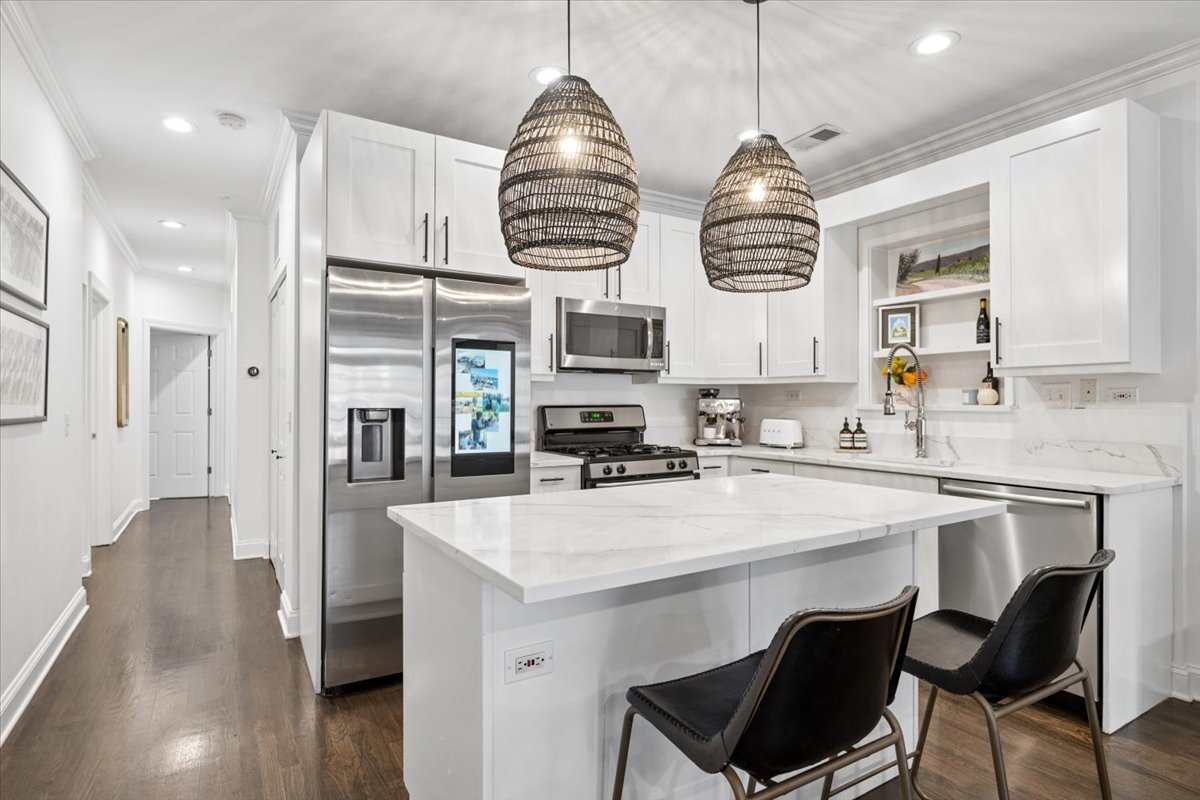 Modern white kitchen with a large island, woven pendant lights and stainless steel appliances.