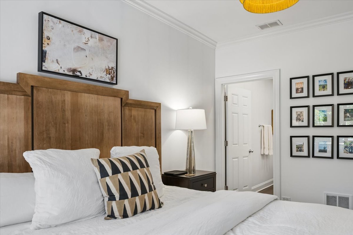 Staged bedroom with a tall wood headboard, white bedding, and framed photos on the wall.