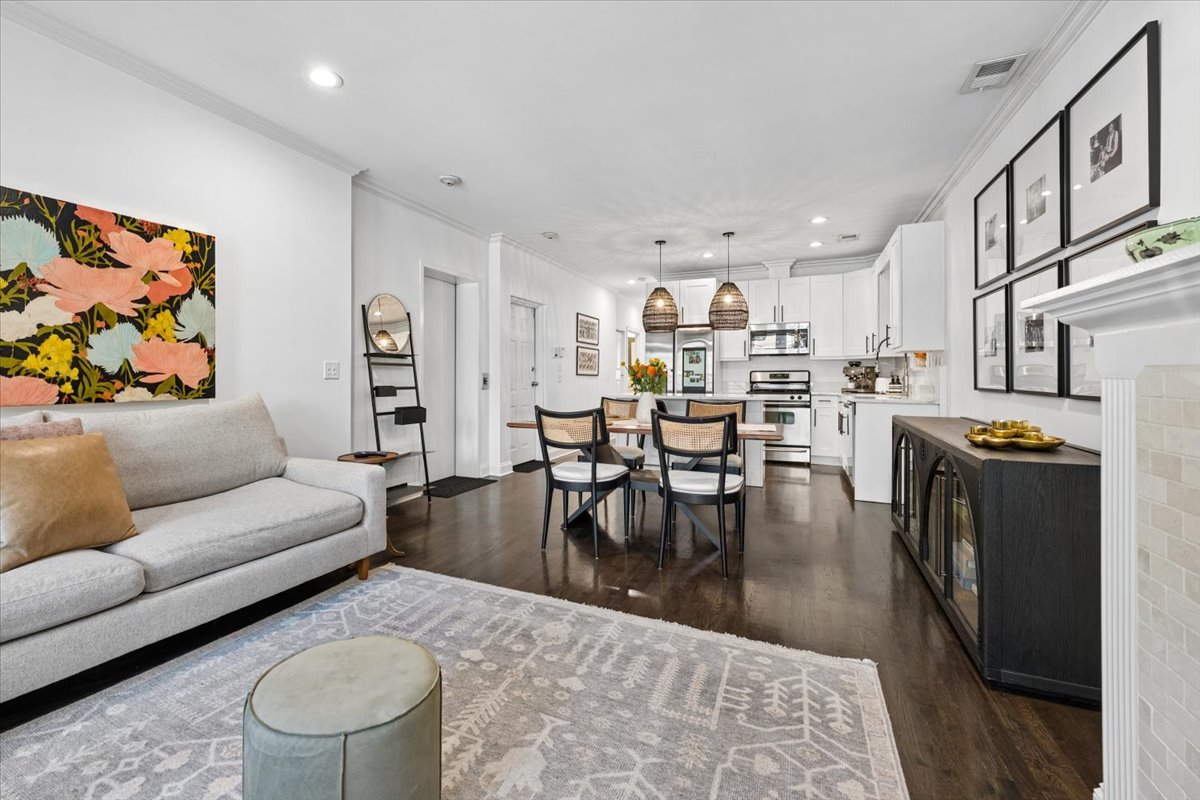Open-plan living and dining area with white kitchen, woven pendant lights, and dark hardwood floors.